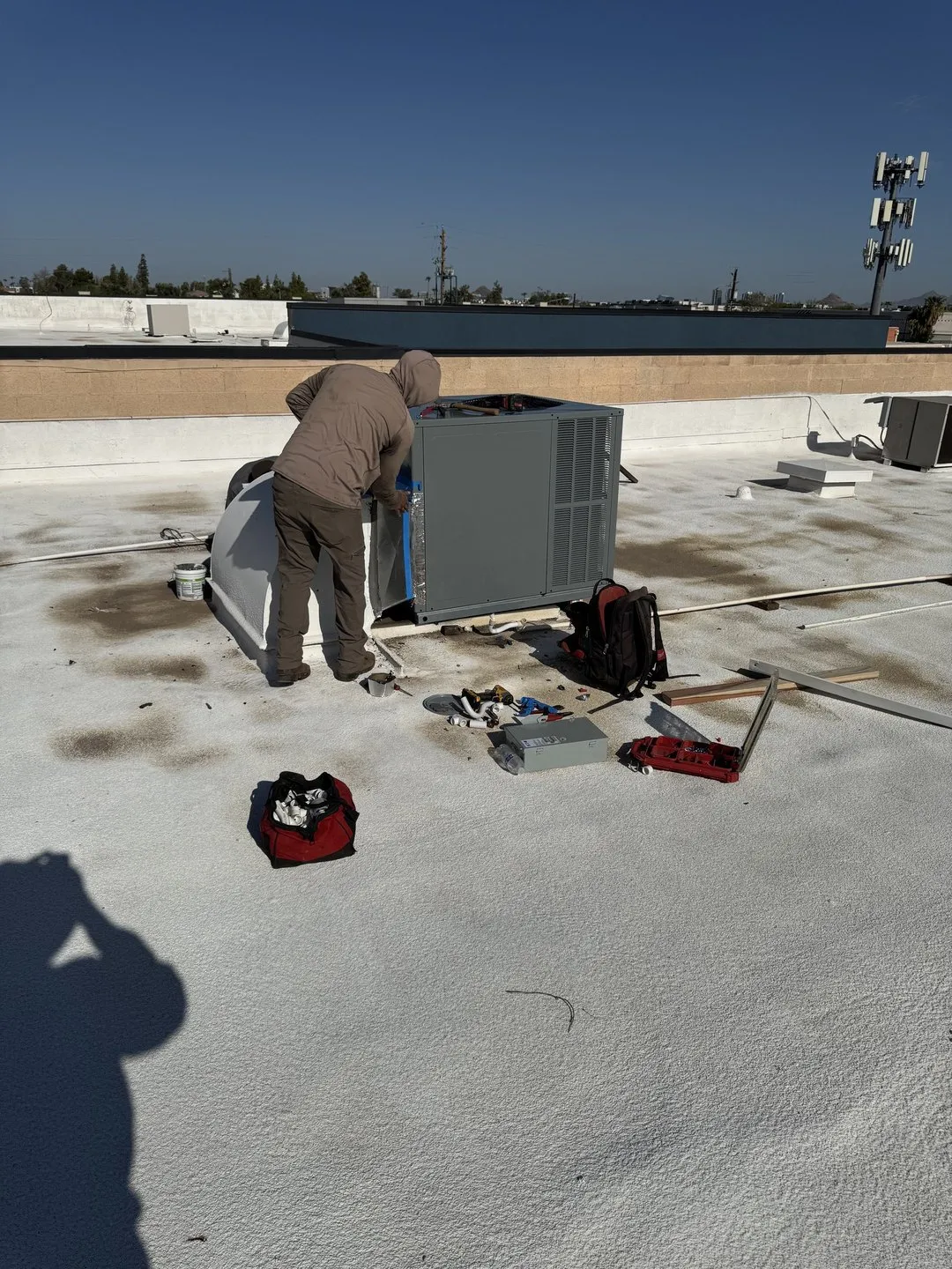 Helping Hands technician servicing a rooftop unit on a flat commercial roof in the Valley