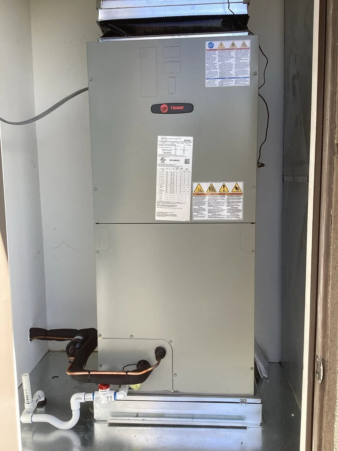 A Trane air handler installed in a hall closet, panel closed, with new refrigerant lines